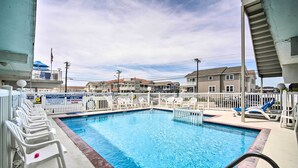 A swimming pool with white chairs, a white fence, and houses in the background. - Walk to Wildwood Beach: Oceanfront Condo w/ View (Wildwood Crest)
