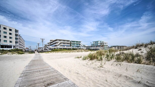 A wooden boardwalk leading to beachfront buildings with multiple balconies and a clear sky. - Walk to Wildwood Beach: Oceanfront Condo w/ View (Wildwood Crest)