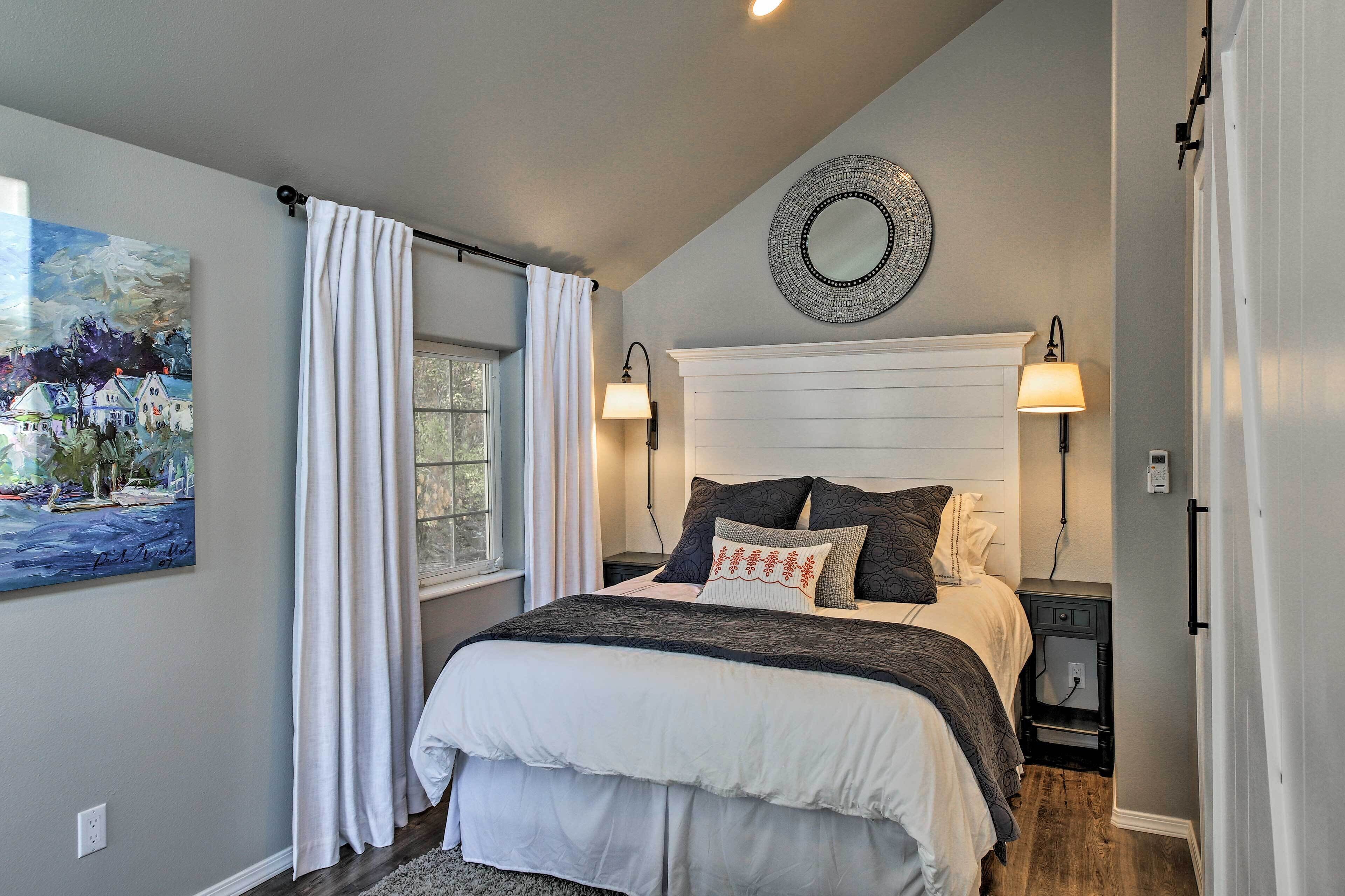 Une chambre à coucher comprenant un lit, des lampes de chevet, une table de chevet, un miroir fixé au mur et une fenêtre avec des rideaux.