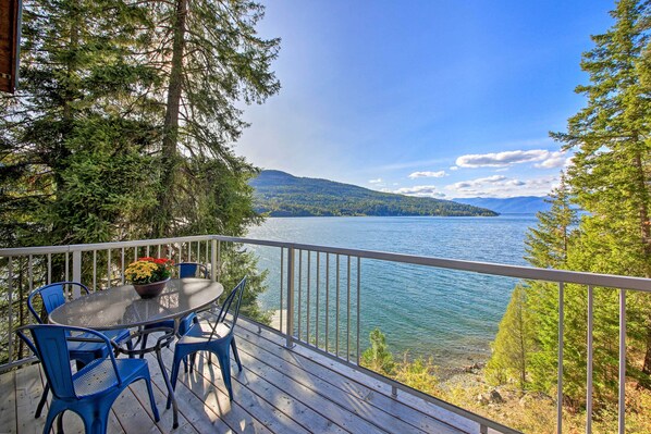 A deck with a table and chairs overlooking a lake, surrounded by trees.