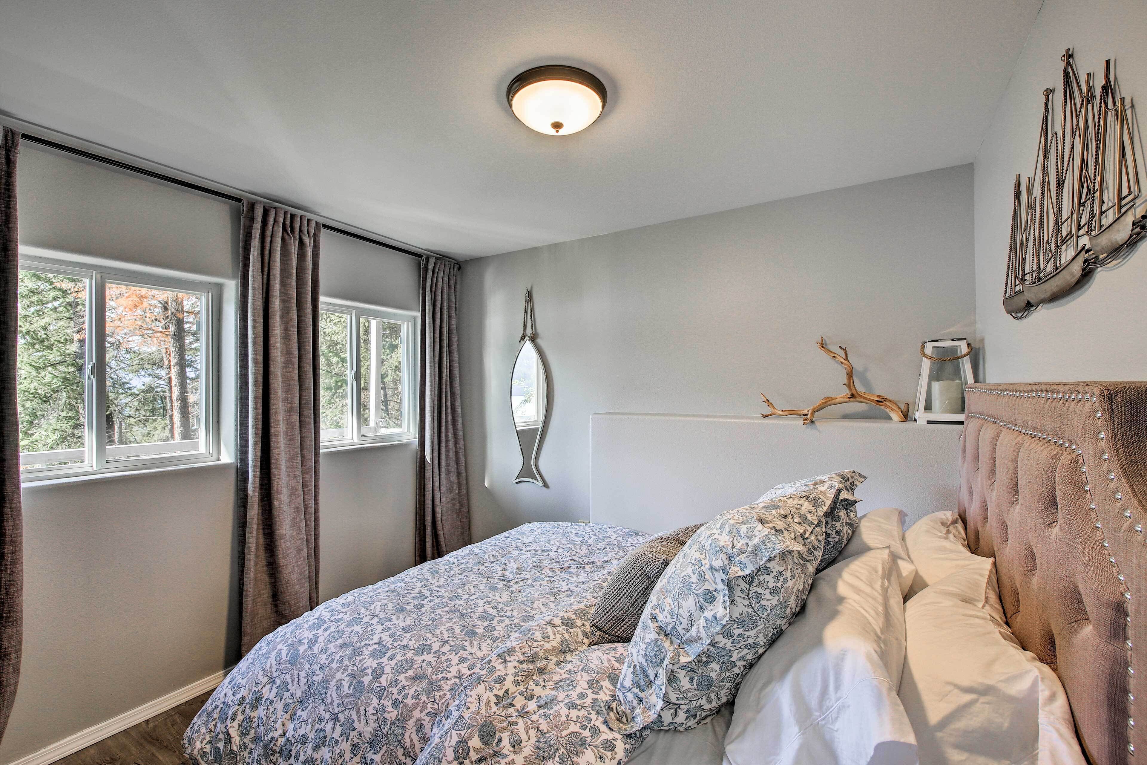 Een slaapkamer met een groot bed, een raam met gordijnen, een wandlamp en een decoratief kunstwerk.