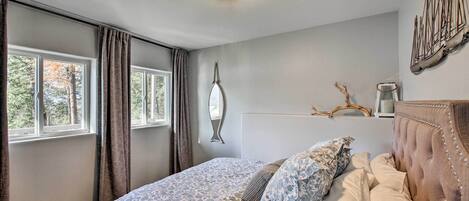 Een slaapkamer met een groot bed, een raam met gordijnen, een wandlamp en een decoratief kunstwerk.