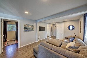 A living room with a sectional sofa, a flat-screen TV mounted on the wall, and a door leading to another room.