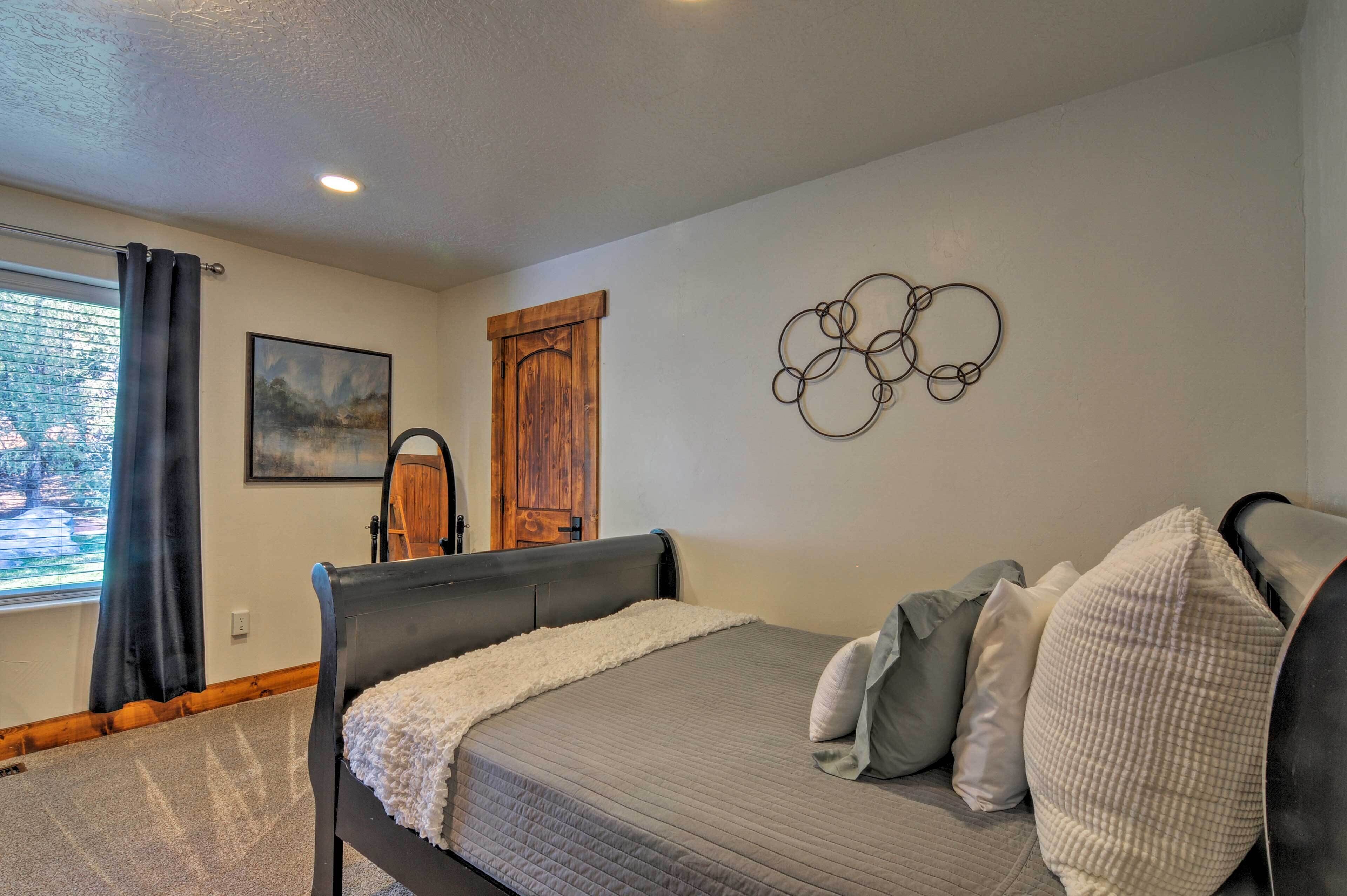 A bedroom with a bed, a window with curtains, a wooden door, and a wall-mounted artwork.