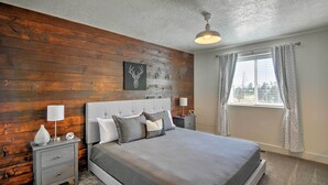 A bedroom with a wooden wall, a bed with grey bedding, two bedside tables with lamps, and a window with curtains. - Luxe Home ~ 2 Mi to Bryce Canyon National Park! (Bryce Canyon)