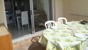 Une terrasse avec une table dressée pour les repas, des chaises et une porte-fenêtre coulissante donnant sur un espace cuisine.