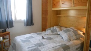 Une chambre à coucher avec un lit, une tête de lit en bois, une table de chevet et une fenêtre avec des rideaux.