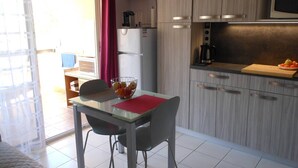 Une cuisine compacte avec un coin repas, comprenant un four à micro-ondes, une machine à café et un saladier de fruits posé sur le comptoir.