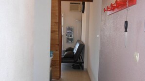 A narrow hallway with a wooden ceiling beam, a black leather sofa in the background, and a red shelf with a light fixture on the right wall.
