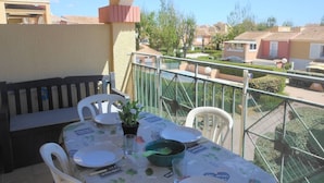 A balcony with a table set for dining, chairs, and a small potted plant.