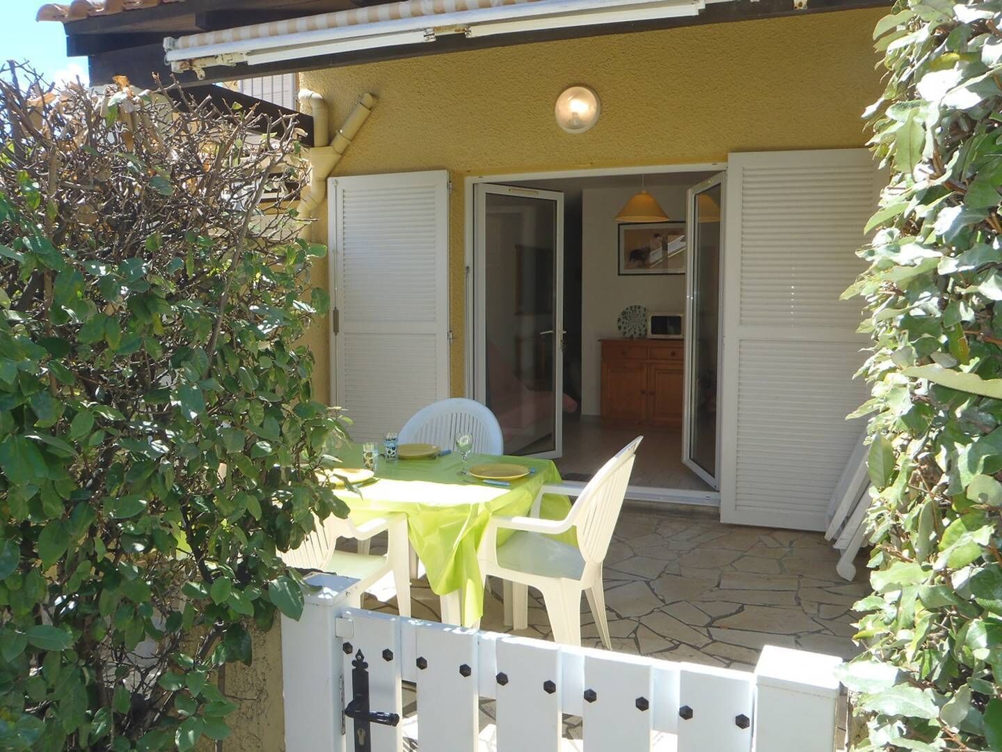 An outdoor patio area with a table and chairs, a white fence, and a door leading to an interior space.