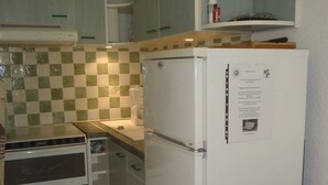 A compact kitchen with a refrigerator, oven, and a tiled backsplash. - APT 3 ROOMS 32m2 + TERRACE 13m2 REF 4050 (MARSEILLAN PLAGE)