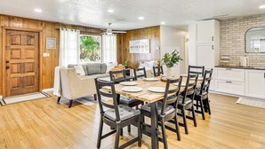 A dining area with a wooden table and chairs, a sofa, and a kitchen area with white cabinets and a brick backsplash. - Charming Canalfront Retreat w/ Double Boat Slip! (Astor)