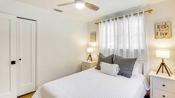 Et soveværelse med seng, sengeborde, ventilator i loftet og gardiner.