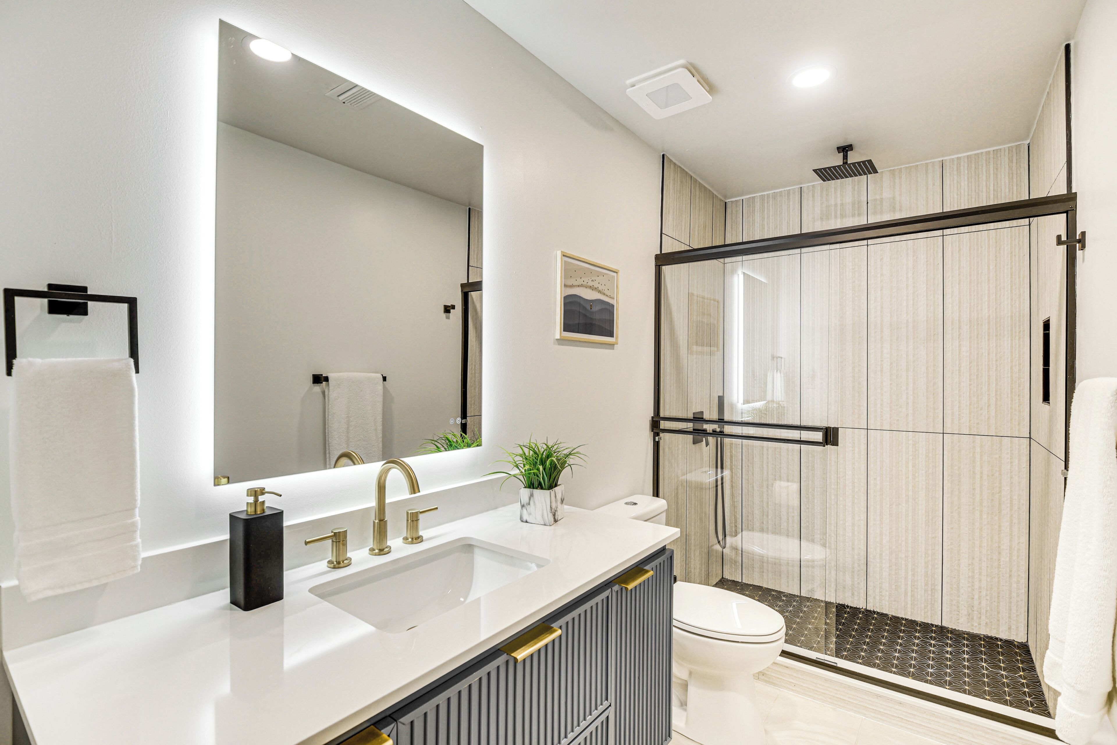 A modern bathroom with a large mirror, a white sink, a toilet, and a glass-enclosed shower area.