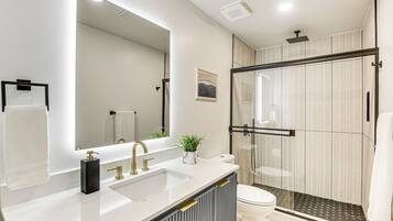 A modern bathroom with a large mirror, a white sink, a toilet, and a glass-enclosed shower area.