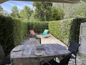 An outdoor patio with a table set for two, two lounge chairs, and a white gate in the background.