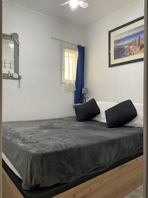 A bedroom with a bed, a window with curtains, a wall-mounted mirror, and a framed picture.