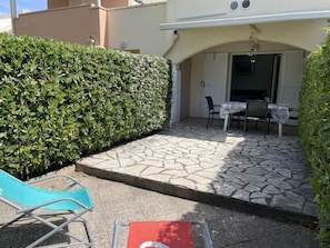 A patio with stone flooring, a table and chairs, and a hedge.