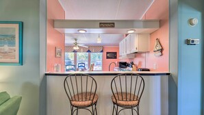 A kitchen with a bar area, two bar stools, a ceiling fan, and a sign that reads "BEACH BUNGALOW". - Atlantic Beach Home w/ Decks & Fire Pit (Atlantic Beach)