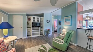 A living room with a green armchair, a white cabinet with shelves, a television, and a ceiling fan. - Atlantic Beach Home w/ Decks & Fire Pit (Atlantic Beach)