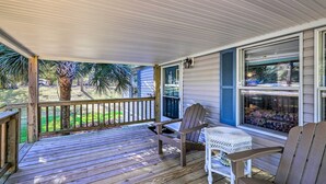 A covered porch with a wooden deck, a white wicker table, and two Adirondack chairs. - Atlantic Beach Home w/ Decks & Fire Pit (Atlantic Beach)