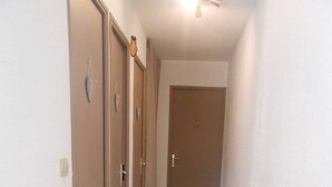 A narrow hallway with wooden flooring and beige walls. There are three doors on the left, one with a heart-shaped decoration above it. The hallway leads to a closed door at the end.
