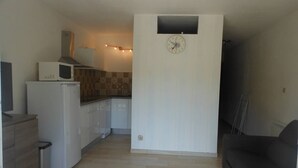 A compact kitchen with a microwave, stove, and sink. A clock is mounted on the wall, and a small window is visible.