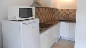 A compact kitchen with a white refrigerator, a microwave, a stove, and a sink. The backsplash has patterned tiles, and the cabinets are white.