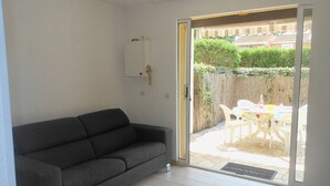 A room with a grey sofa, a sliding glass door leading to an outdoor patio with a table and chairs.