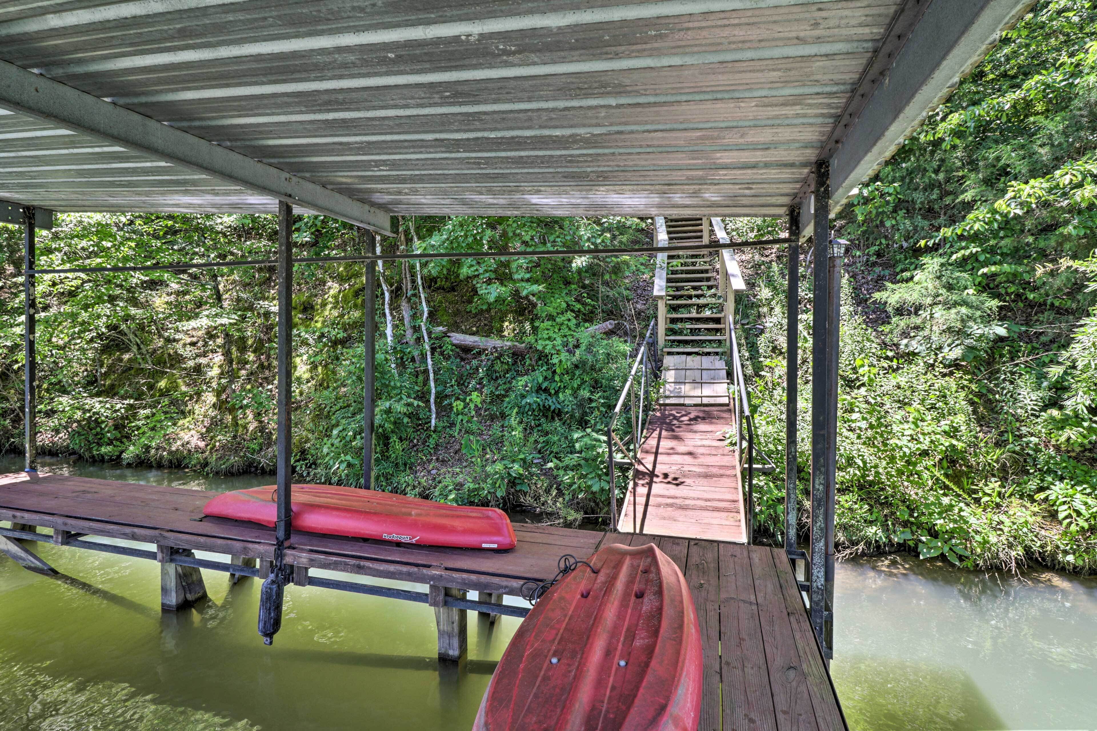 Un muelle de madera cubierto con un kayak y una canoa, ambos rojos, rodeado de vegetación exuberante y una pequeña escalera que conduce a una plataforma superior.