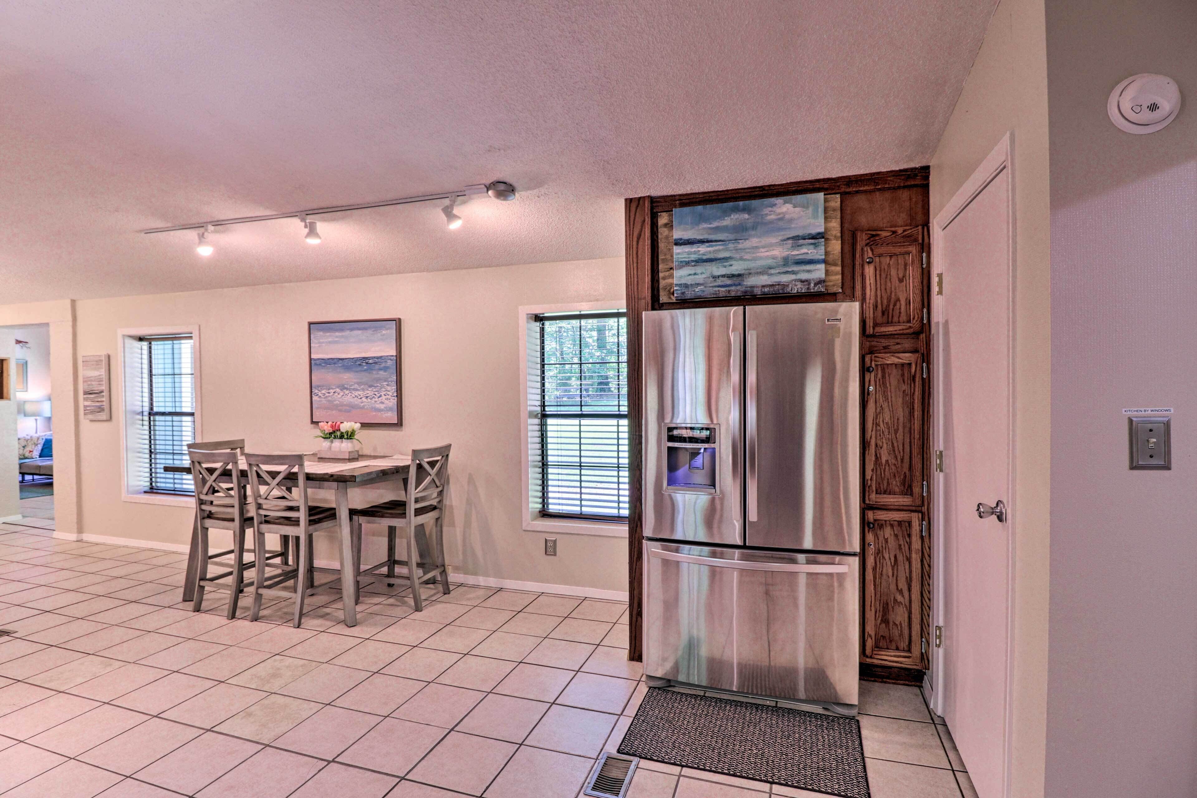 A kitchen with a stainless steel refrigerator, wooden cabinets, a dining table with chairs, and a window with blinds.