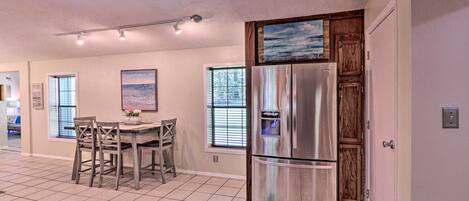 A kitchen with a stainless steel refrigerator, wooden cabinets, a dining table with chairs, and a window with blinds.