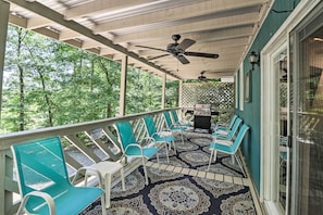 A covered porch with ceiling fans, outdoor seating, and a view of the surrounding trees.