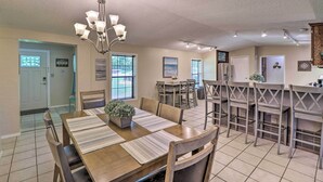 Un grand espace dédié à la salle à manger, avec une table et des chaises en bois, un lustre, et un coin cuisine doté de tabourets de bar.