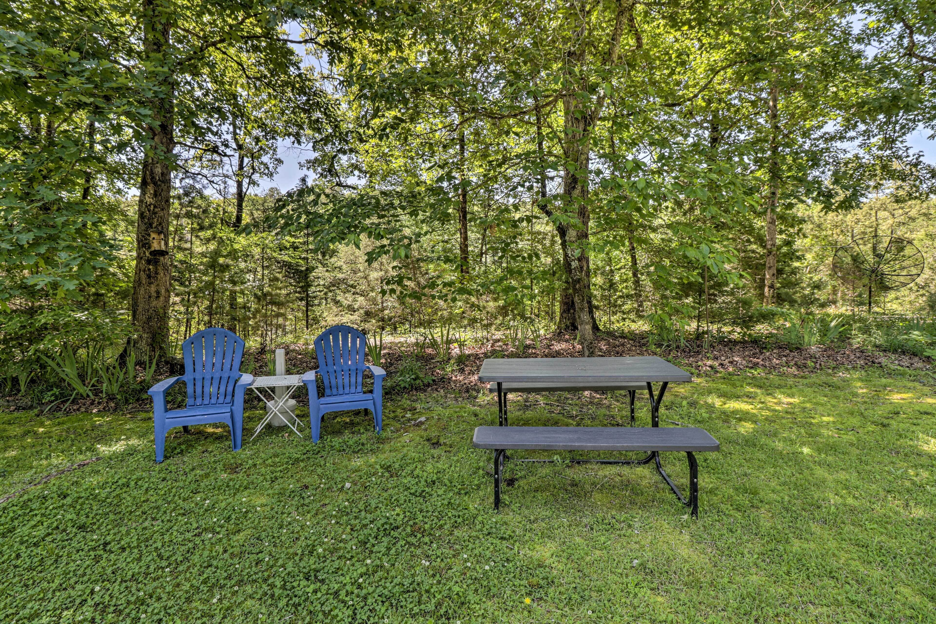 A picnic setup with two blue chairs and a table in a grassy area surrounded by trees.