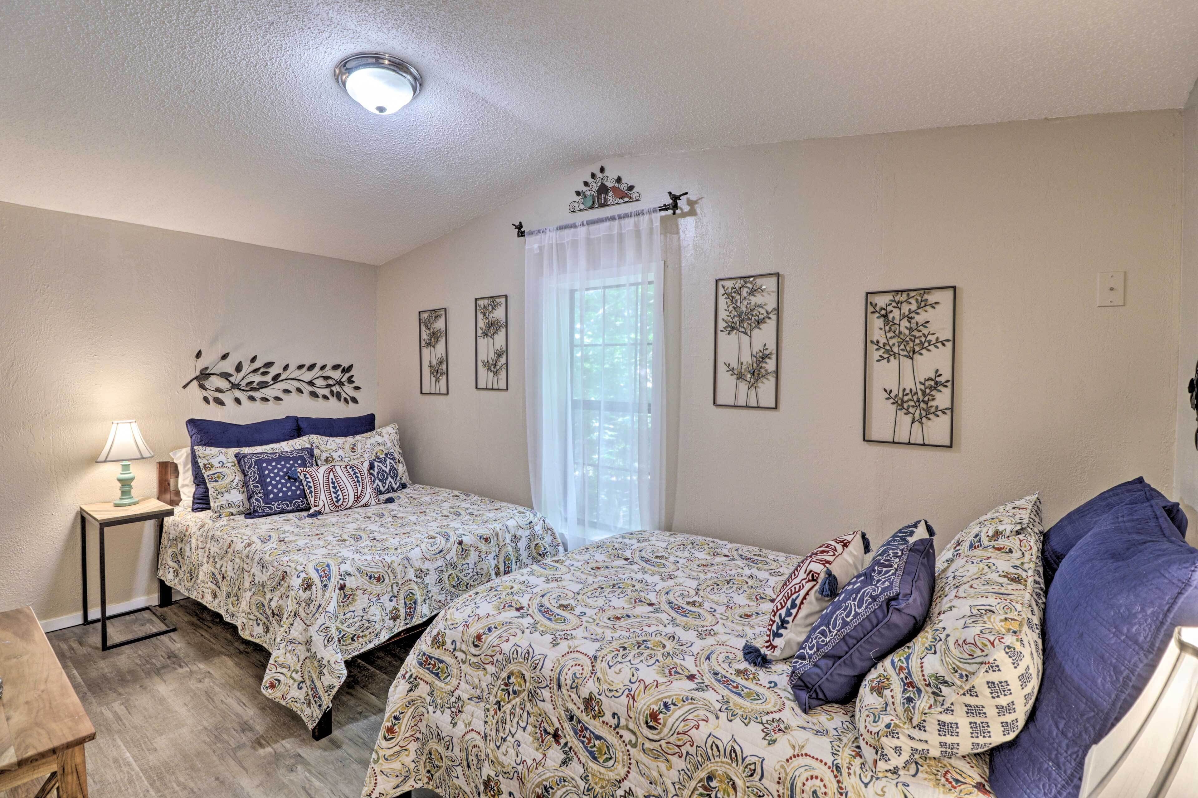 A bedroom with two beds, a nightstand, a lamp, and wall art.