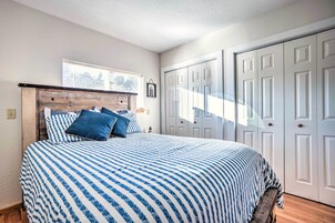 Un dormitorio con cama, cabecera de madera, ventana y puertas blancas.