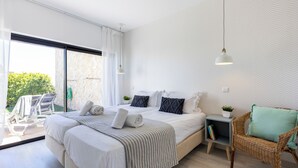 A modern bedroom with a large bed, a wicker chair, and a view of the outdoors.