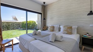 A modern hotel room with a large bed, a view of the outdoors, and a small bedside table with books.