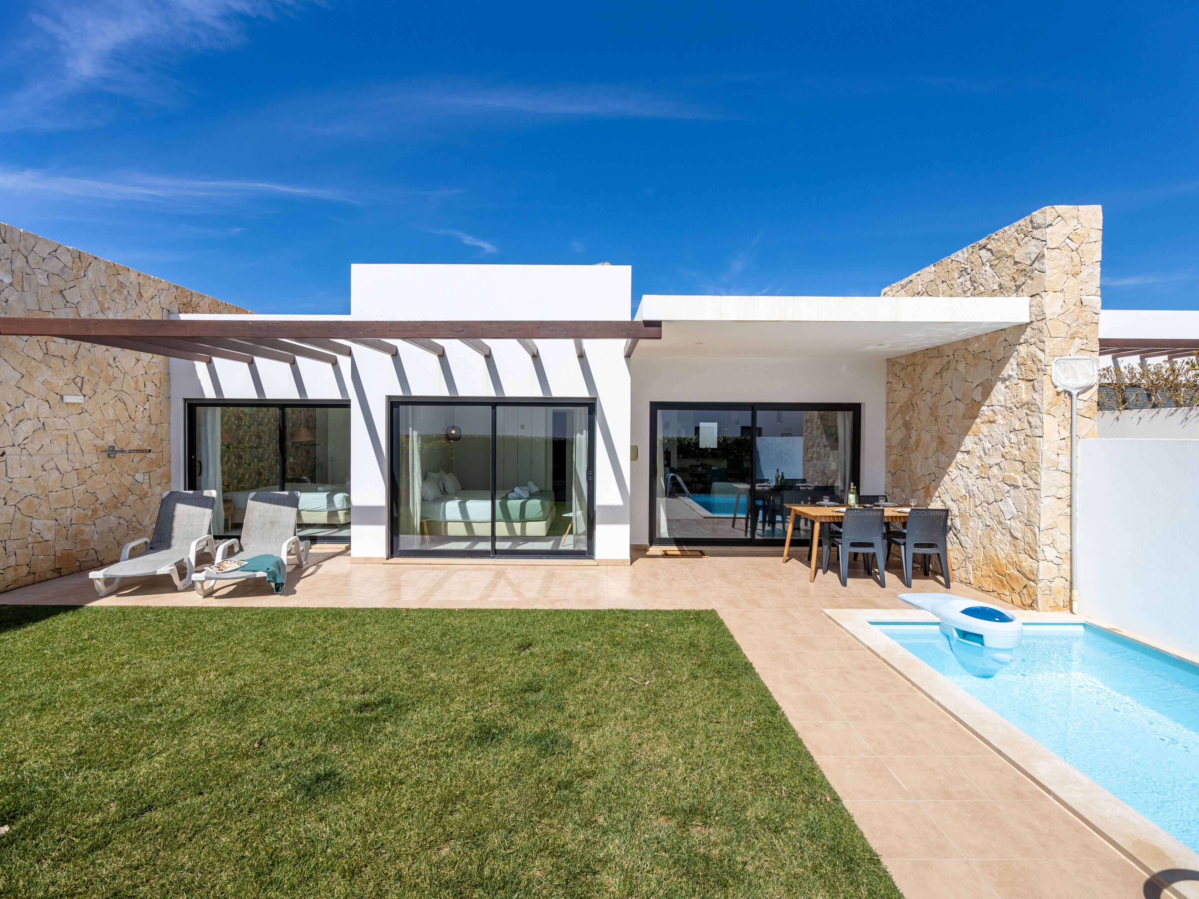Ein modernes Haus mit Swimmingpool, einer Terrasse mit Stühlen und einem grünen Rasen.