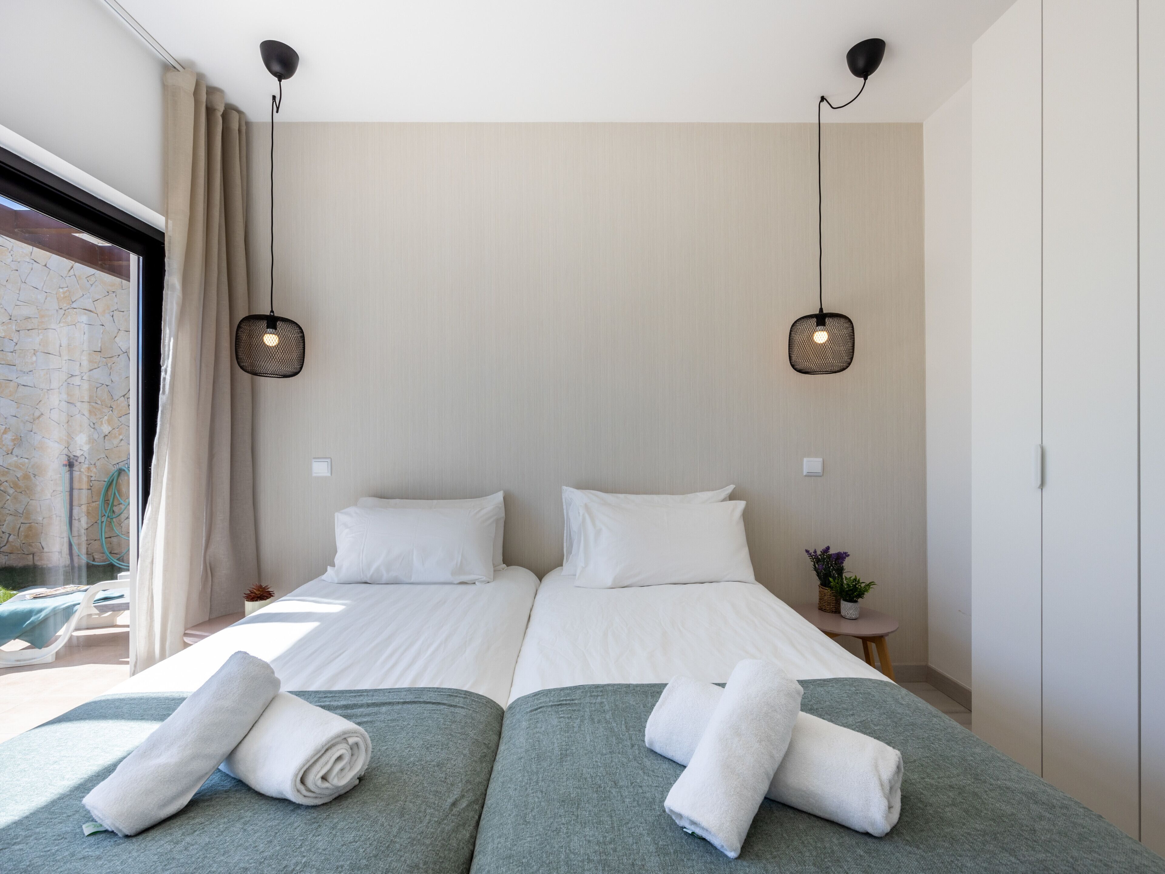 Moderni hotellihuone, jossa on kaksi sänkyä, suuri ikkuna, jossa on verhot, ja kaksi riippuvalaisinta.