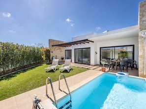 Ein moderner Poolbereich im Freien mit Terrasse, Liegestühlen und Esstisch.