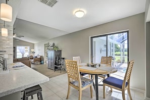 A modern kitchen with a marble countertop, wooden chairs, and a dining table.