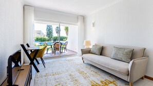 Ein modernes Wohnzimmer mit einer Couch, einem Esstisch mit Stühlen und Blick auf einen Pool und Grünflächen.