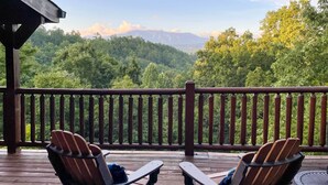 A wooden deck with two Adirondack chairs facing a forested mountain backdrop.