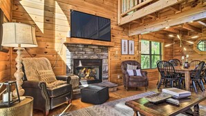 A cozy cabin interior with a fireplace, wooden walls, a television, and a dining area.