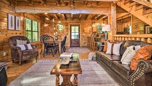 A log cabin interior with a dining area, a sofa, a coffee table, and a staircase.