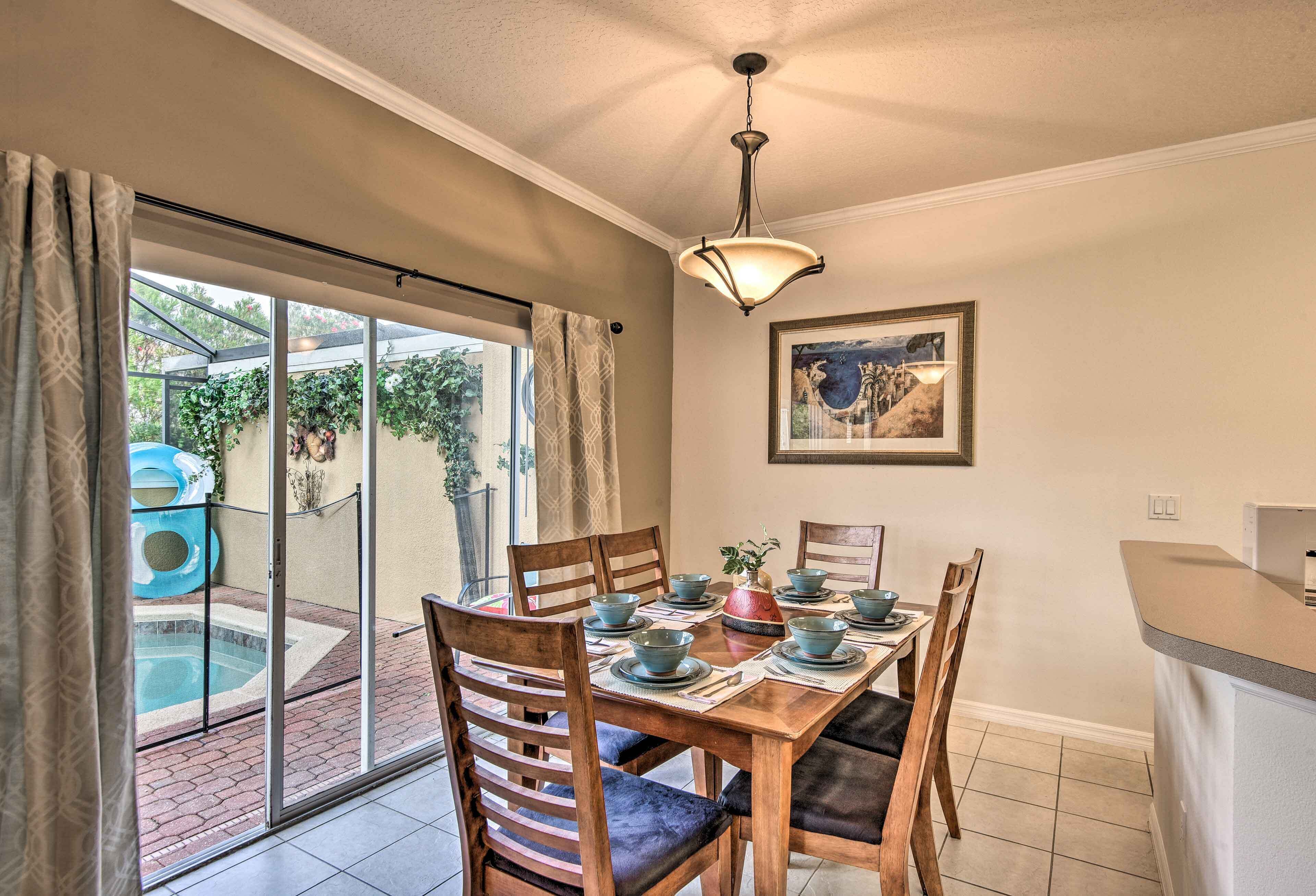A dining area with a table set for six, surrounded by wooden chairs with cushioned seats. A glass door leads to a pool area with a hot tub.