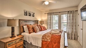 Une chambre à coucher avec un lit, des tables de chevet, un ventilateur de plafond et une fenêtre avec des rideaux.